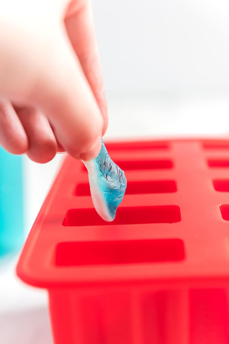 A hand adding a gummy shark into a red popsicle mold