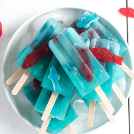 A pile of blue lemonade popsicles with Swedish fish inside on a bowl of ice