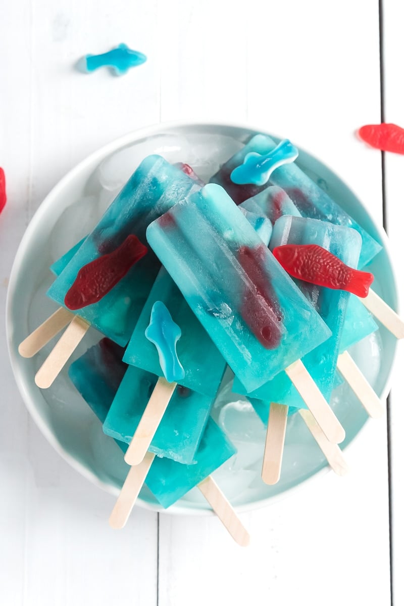 A pile of blue lemonade popsicles with Swedish fish inside on a bowl of ice