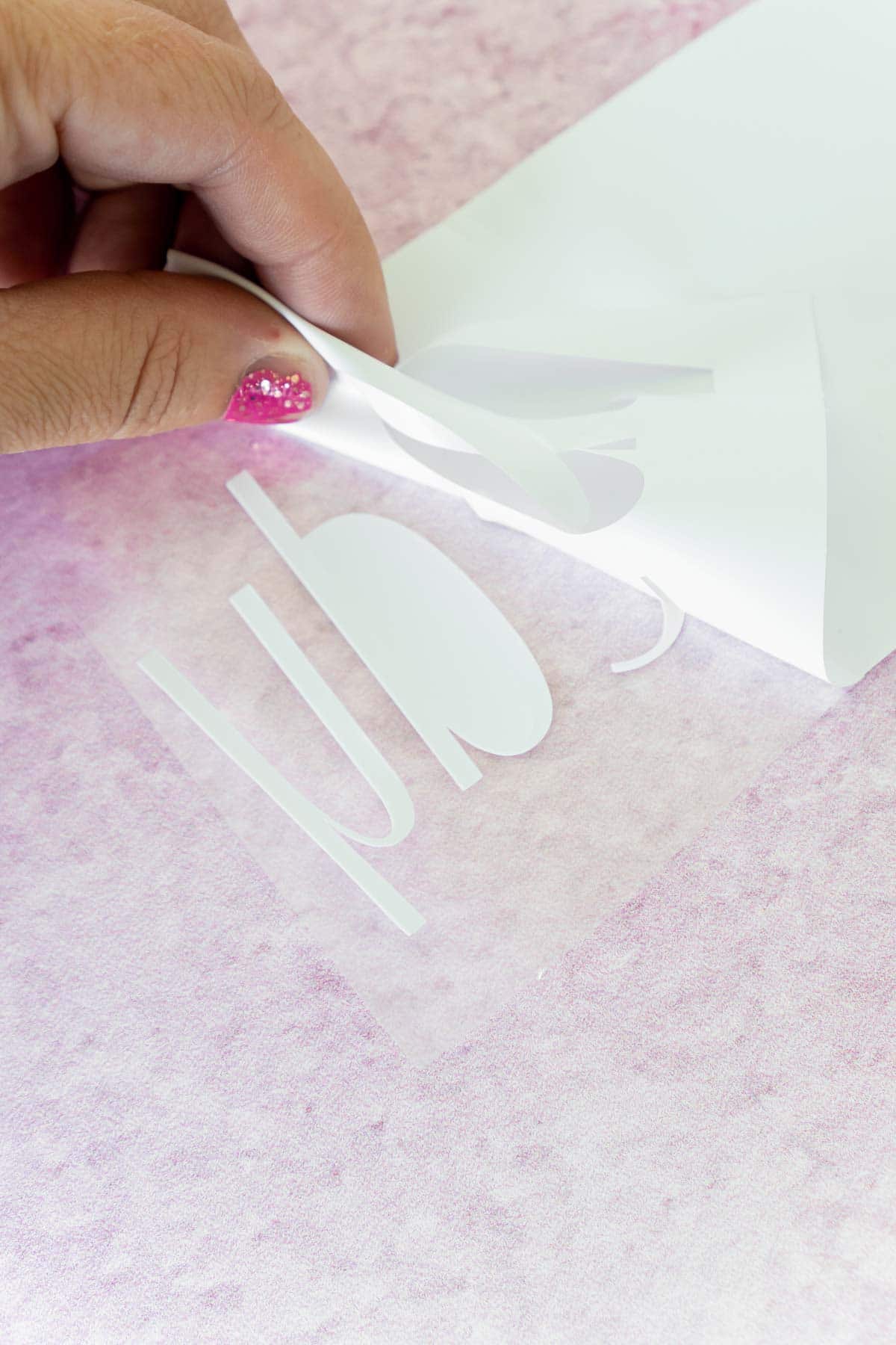 Woman's hand pulling back vinyl from white iron on vinyl