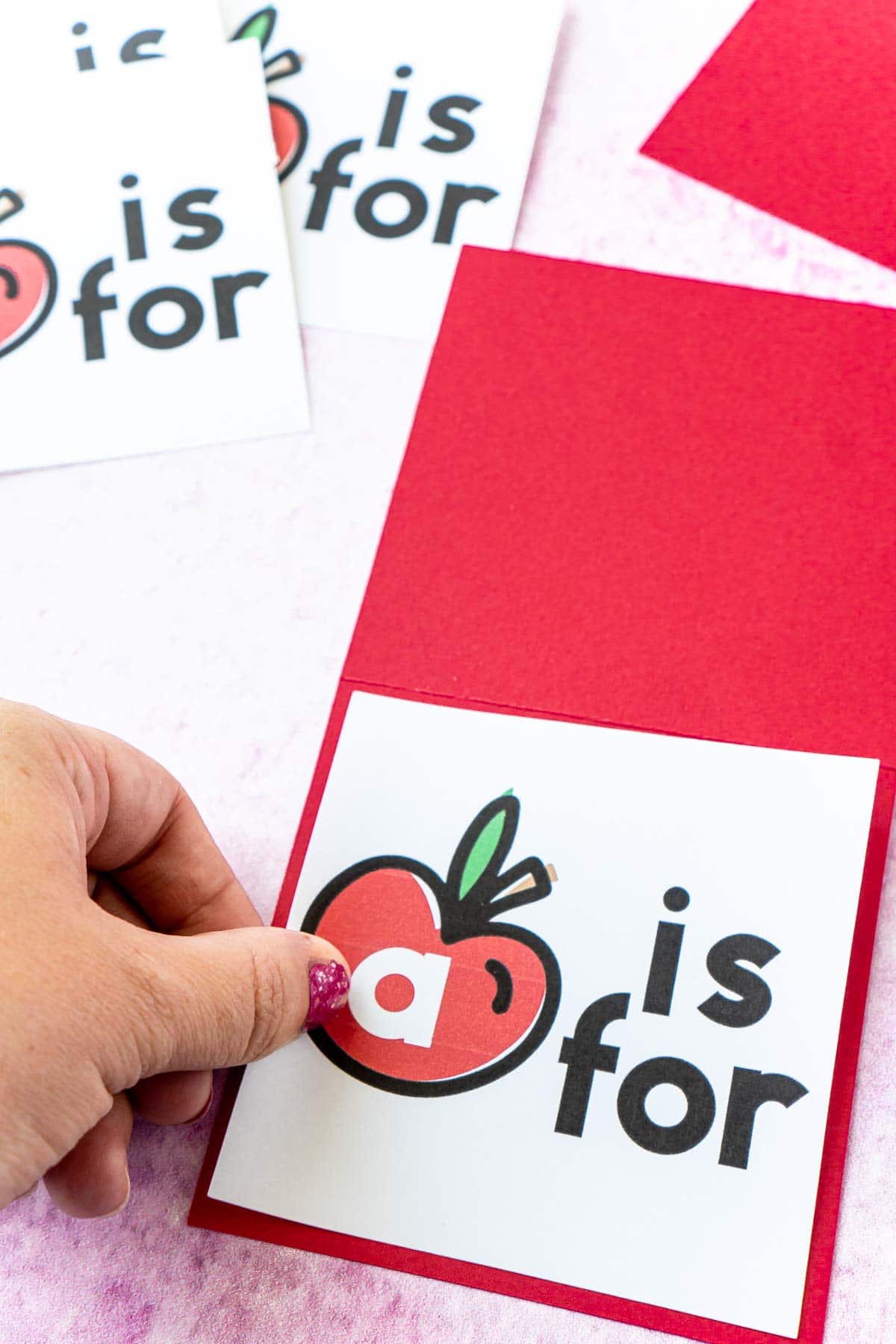 Woman's hand adding an apple card to a piece of red cardstock