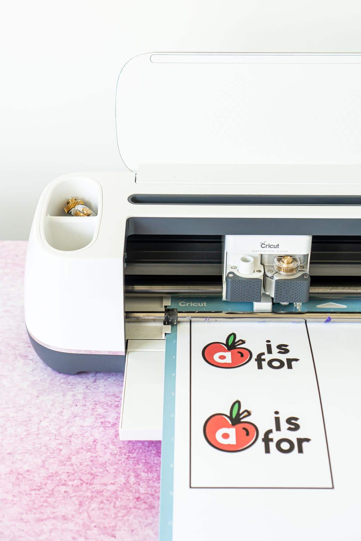 Cricut Maker with a white card apple card on a blue mat