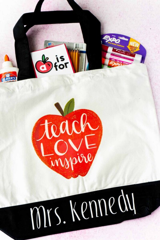 A tote bag with an apple and school supplies sticking out