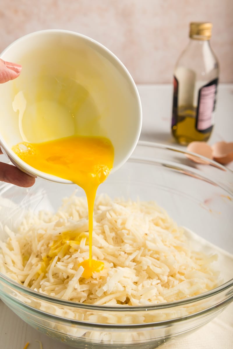 Woman pouring an egg into a bowl of hash browns