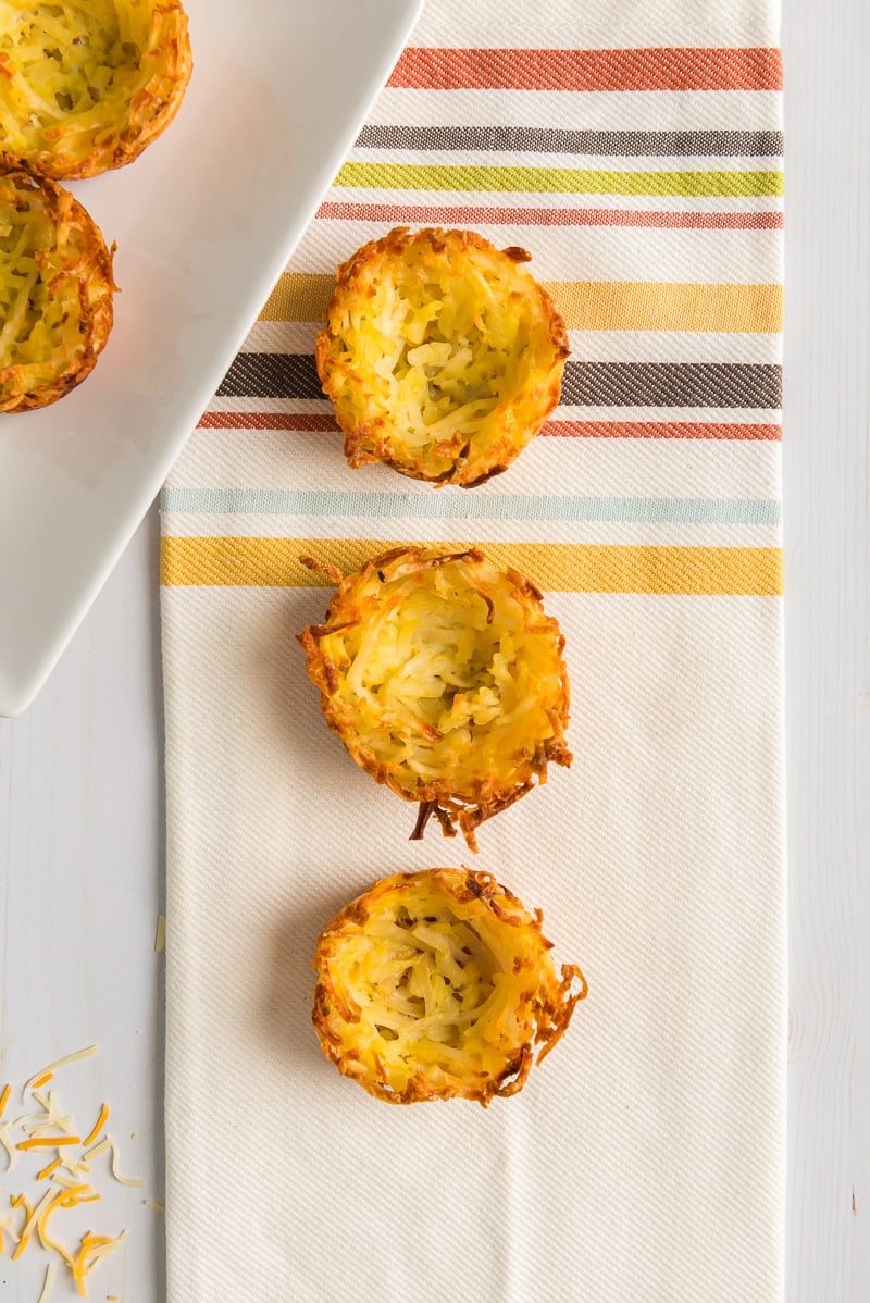 Three hash brown cups lined up on a white napkin with stripes