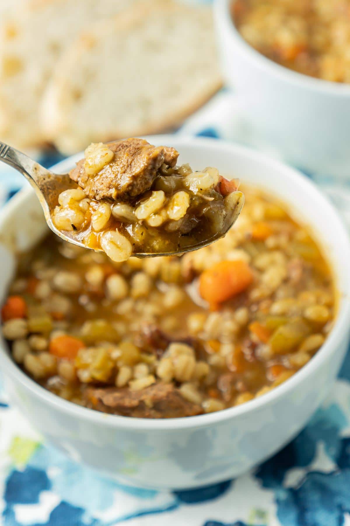 Spoon of beef barley soup above a bowl of beef and barley soup