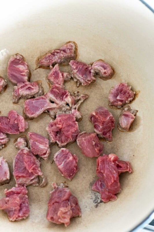 Pieces of stew meat browning in a ceramic pot