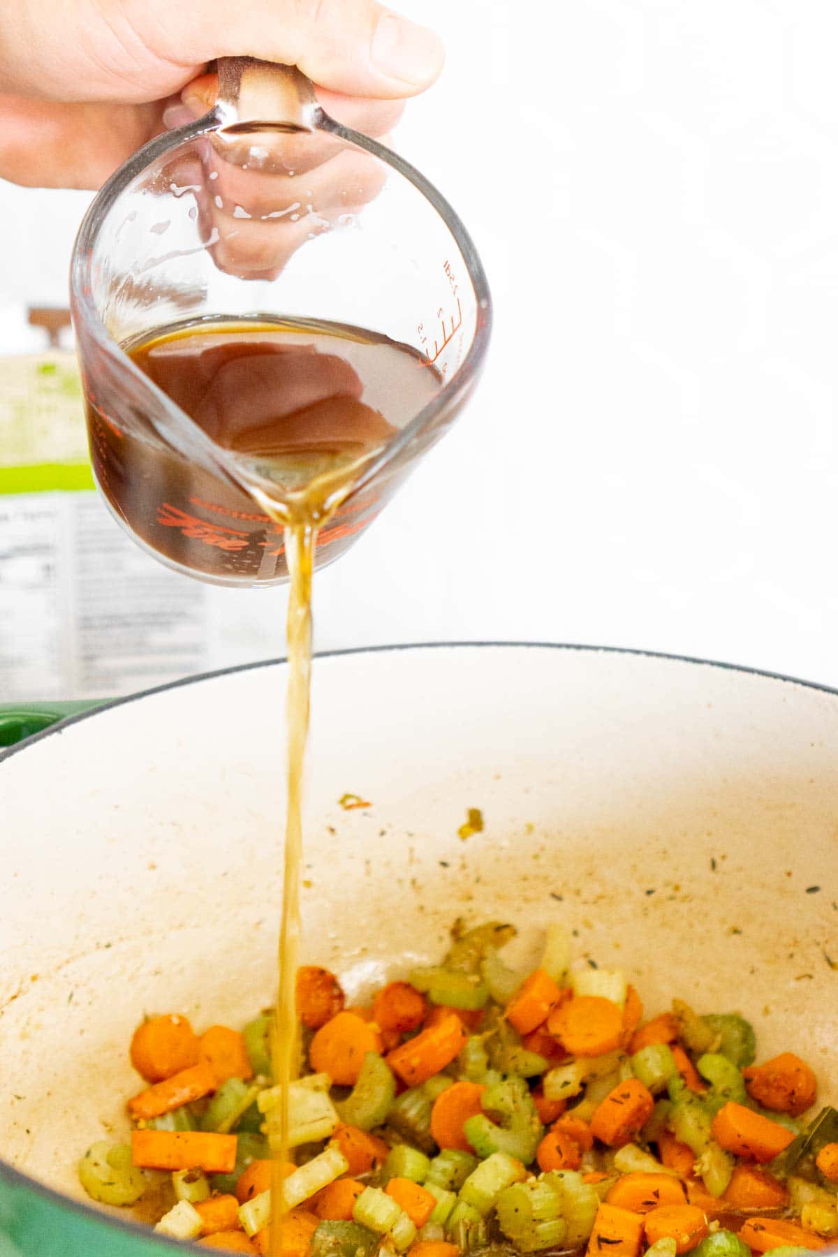 Man's hand pouring beef broth into beef barley soup