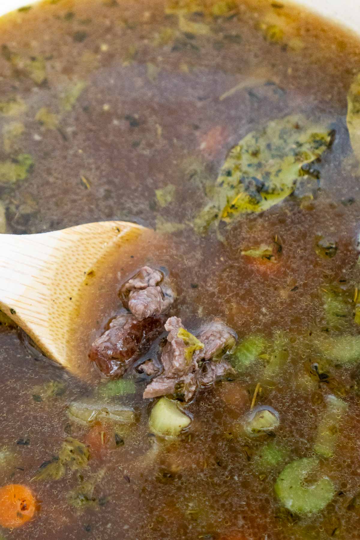 Wooden spoon stirring in beef in a beef and barley soup