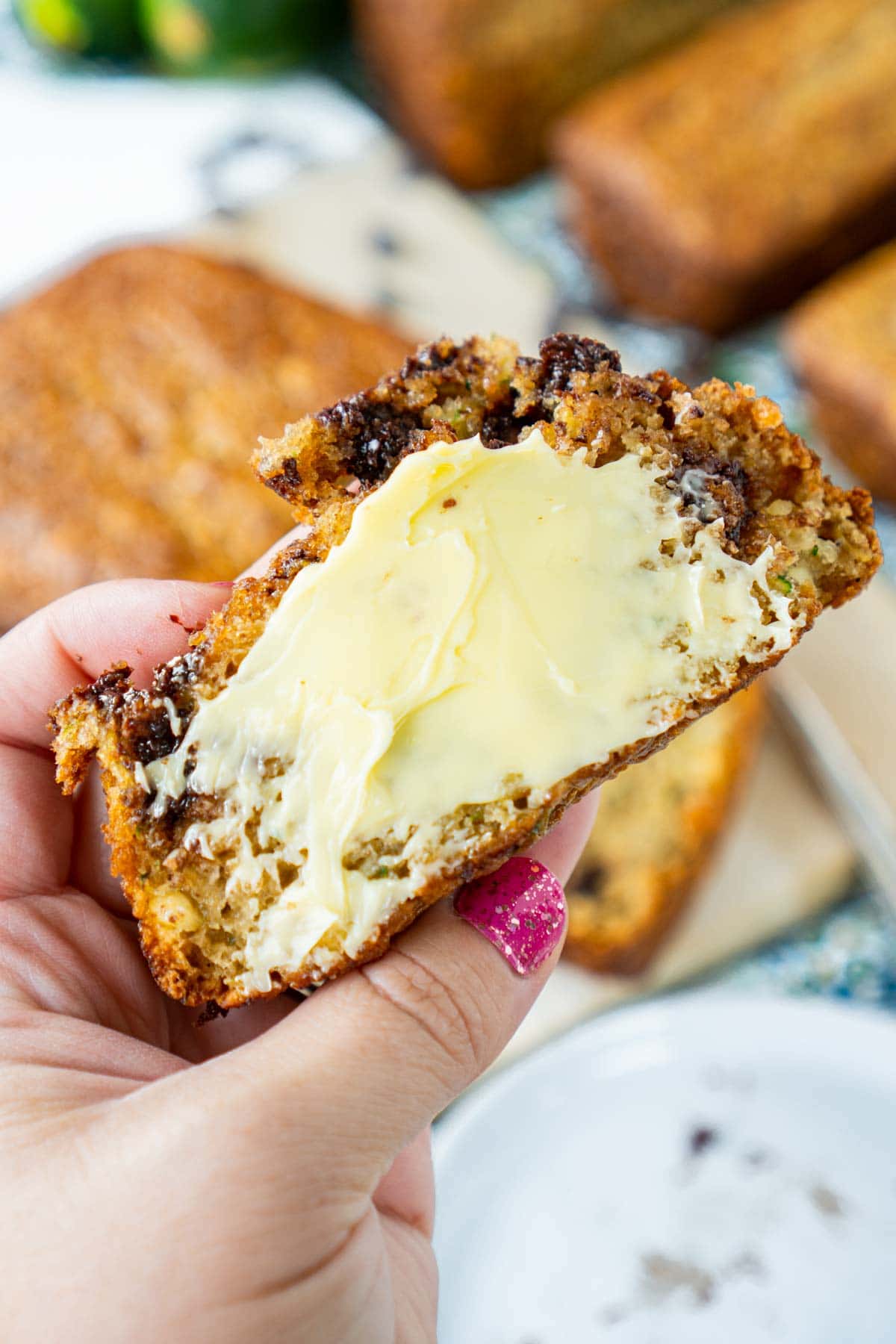 A woman's hand holding a piece of chocolate chip zucchini bread slatered with butter