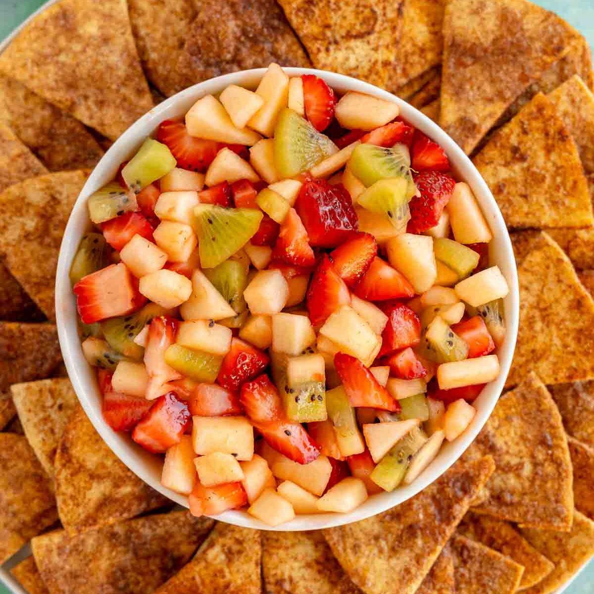 white bowl filled with fruit salsa with cinnamon chips around it
