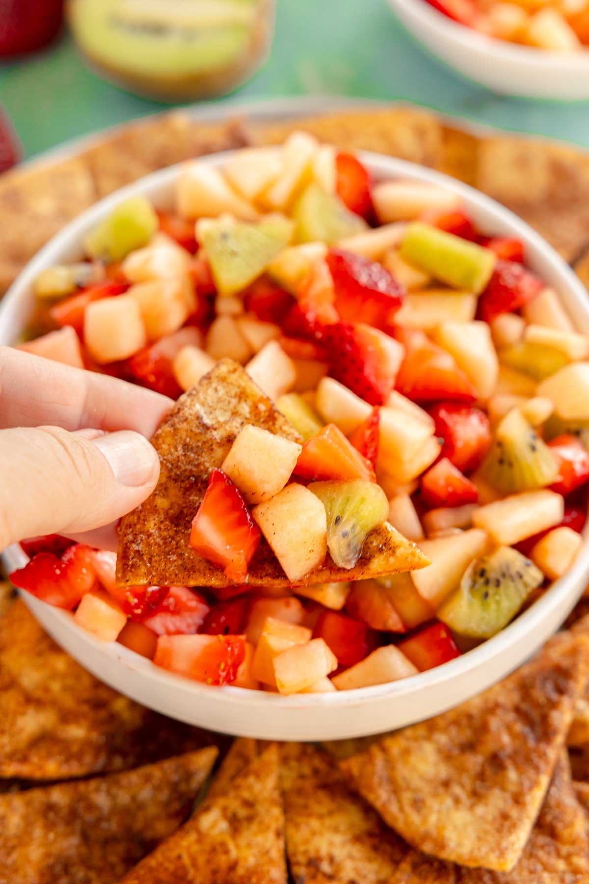 hand holding a cinnamon chip topped with fruit salsa