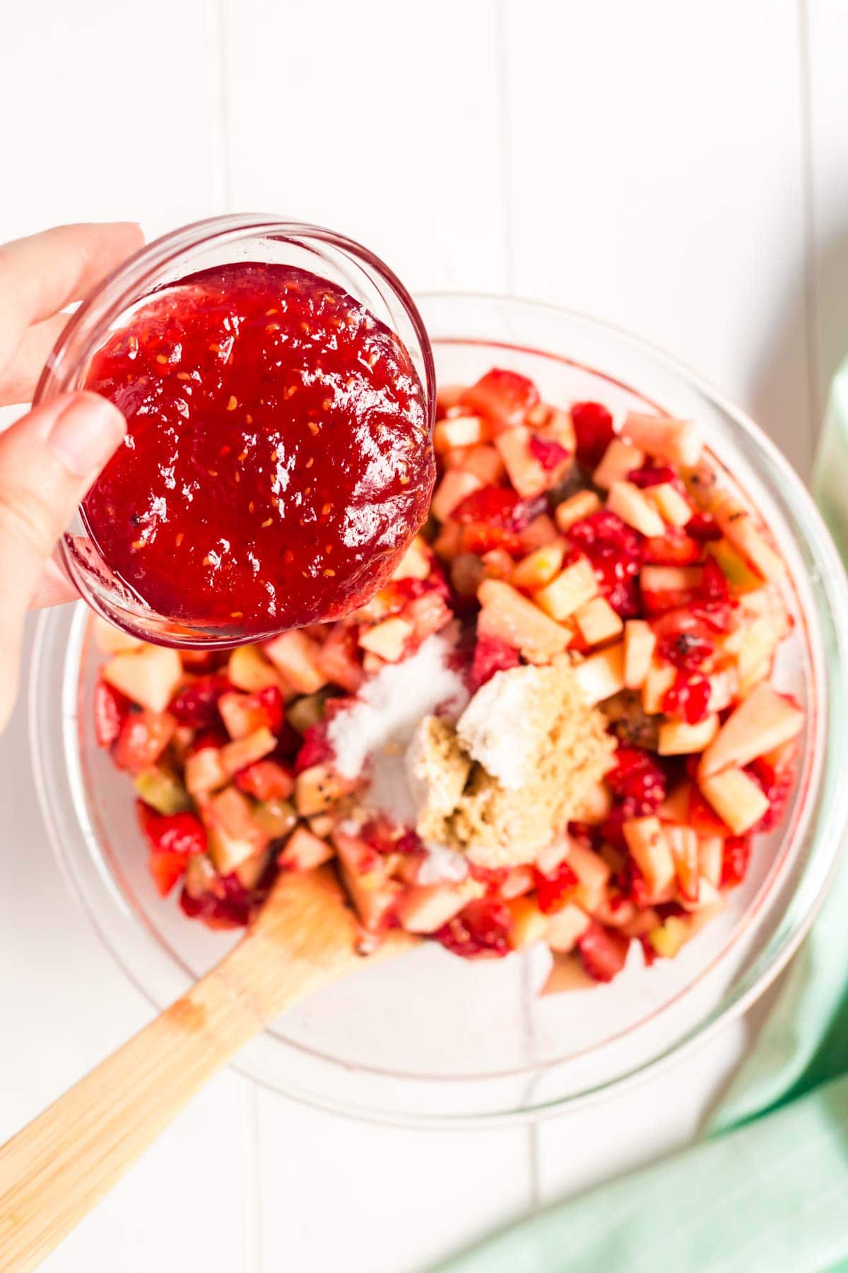 Hand holding a glass bowl of jam over top of a bowl of fruit salsa