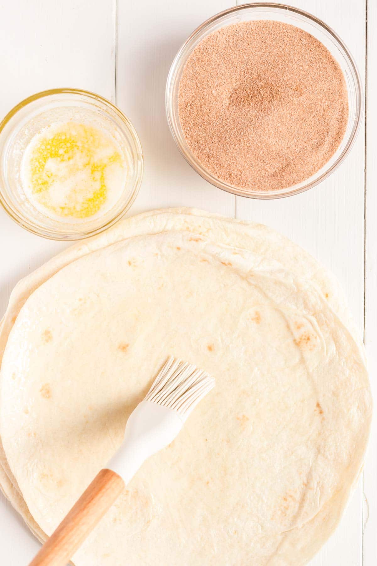 Silicone brush with a stack of tortillas and a bowl of melted butter and cinnamon sugar