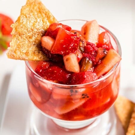 A small glass cup of fruit salsa with a cinnamon chip stuck in it