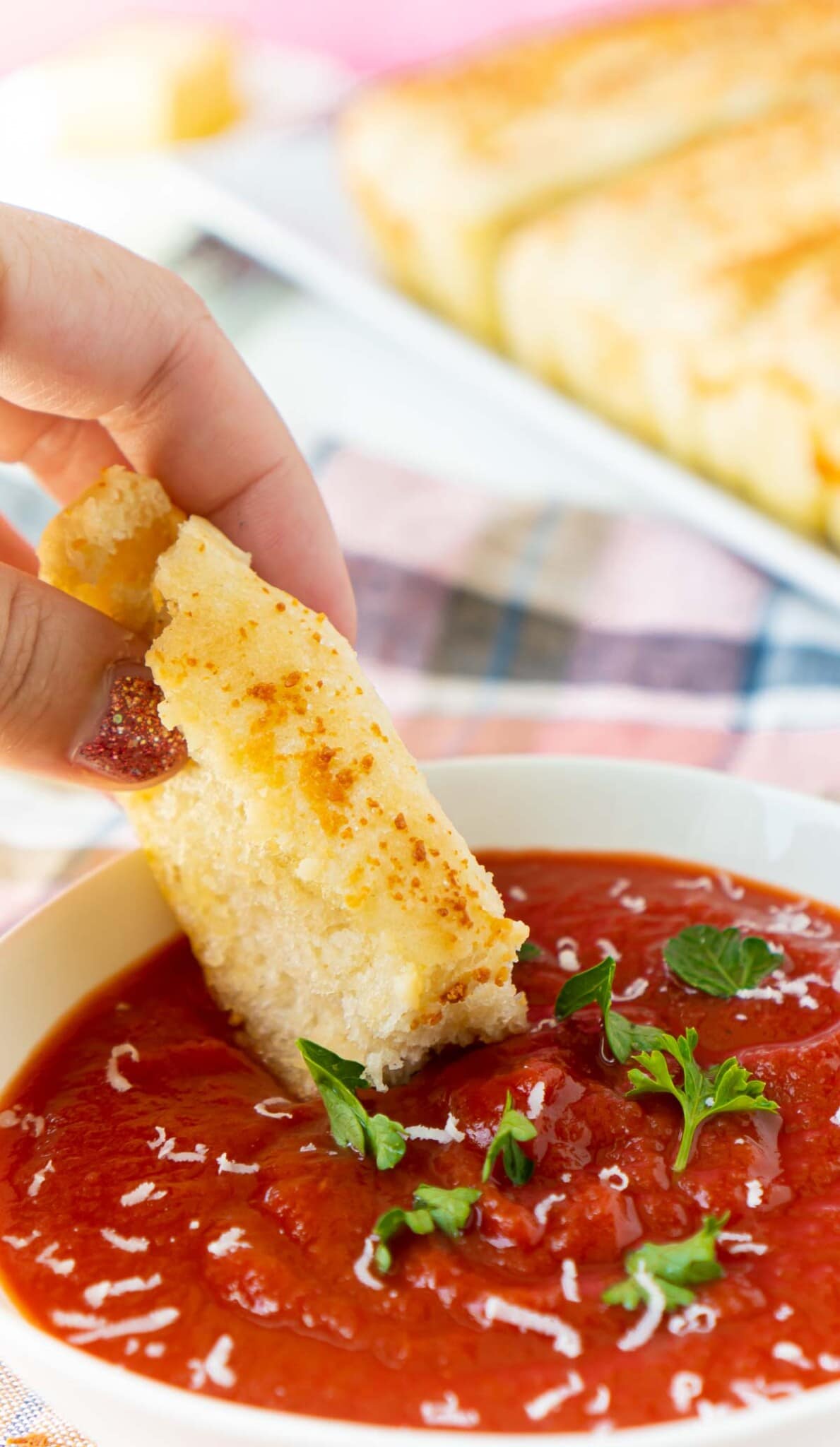 Woman's hand dipping a garlic breadstick into a bowl of red marinara sauce