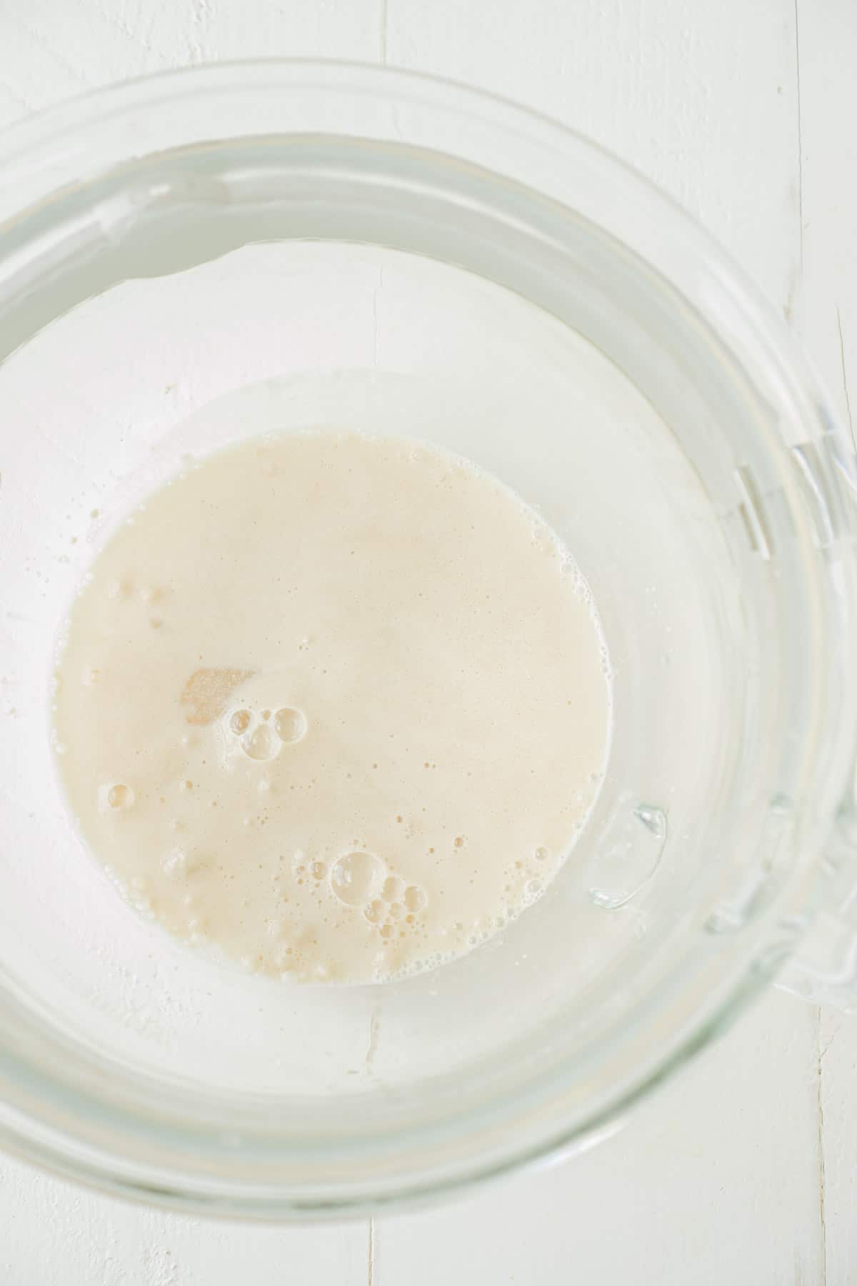 A glass mixing bowl with yeast, water, and sugar.