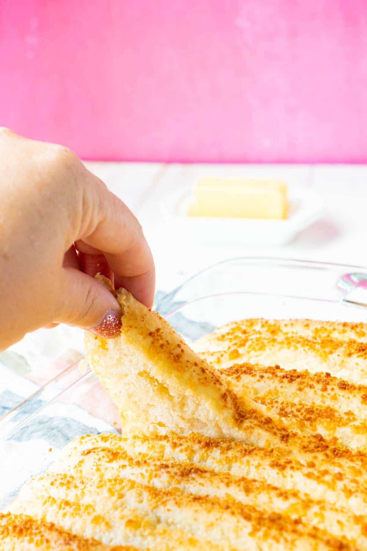 A woman's hand pulling a single garlic breadstick out of a pan of garlic breadsticks