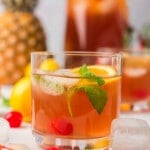 Glass of fruit punch in front of a pitcher of fruit punch with fruit all around