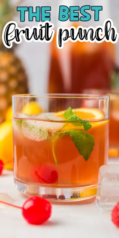 Glass of fruit punch in front of a pitcher of fruit punch with fruit all around with text for Pinterest