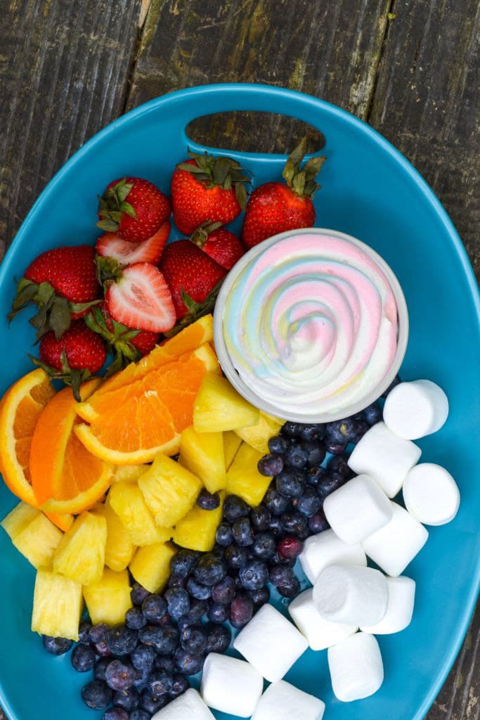 A blue bowl with fresh fruit and a rainbow colored fruit dip