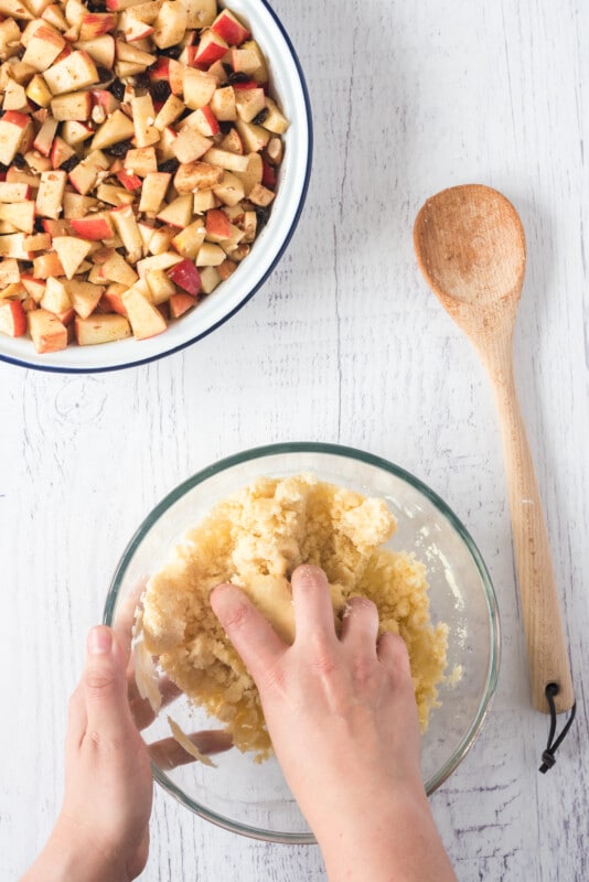 Hand kneading an apple crumble topping in a glass bowl