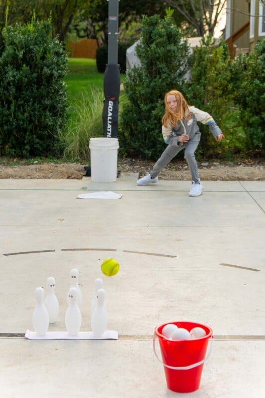 Girl bowling a baseball at bowling pins