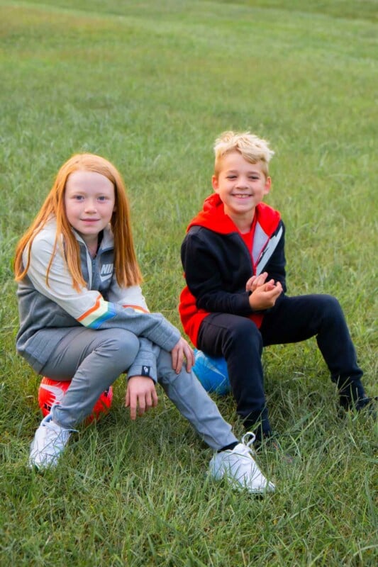 Kids sitting on soccer balls in a grassy field