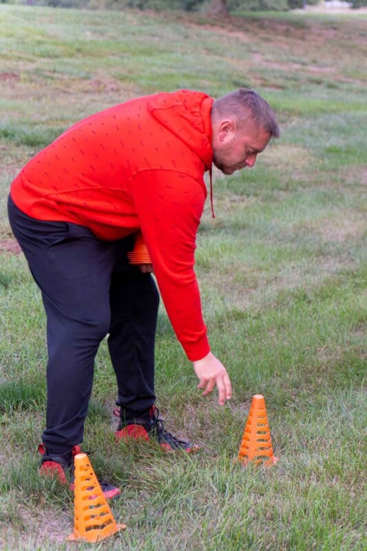 An adult setting up a cone in a grassy field