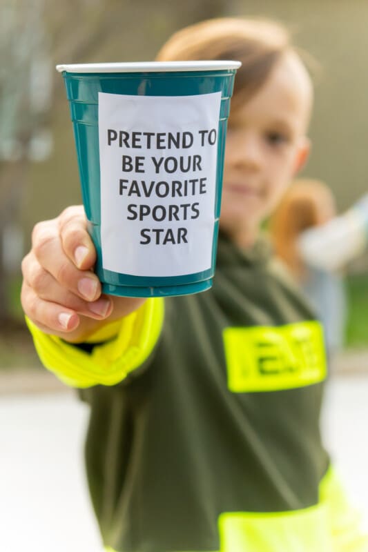 Kid holding a plastic cup that says pretend to be your favorite sports star