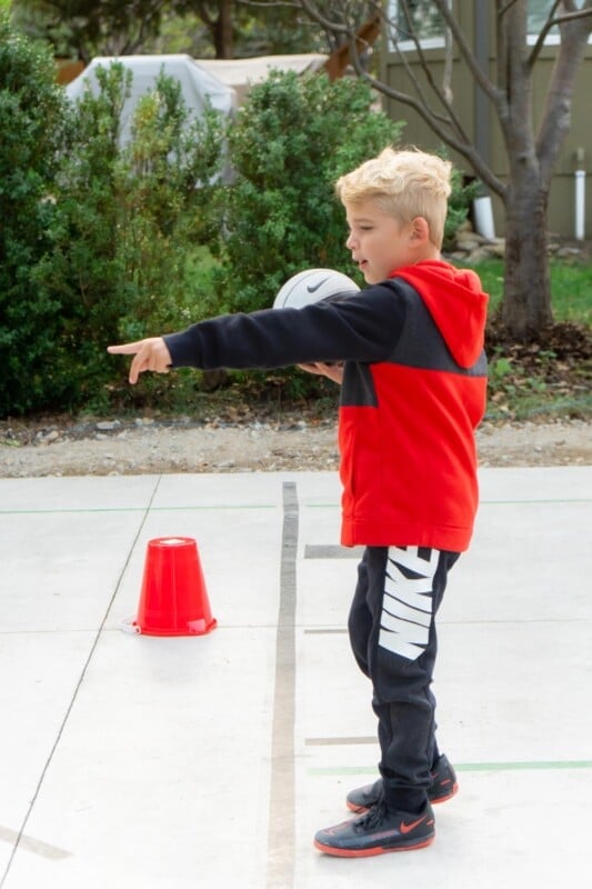 Boy holding a ball pointing at things on the ground