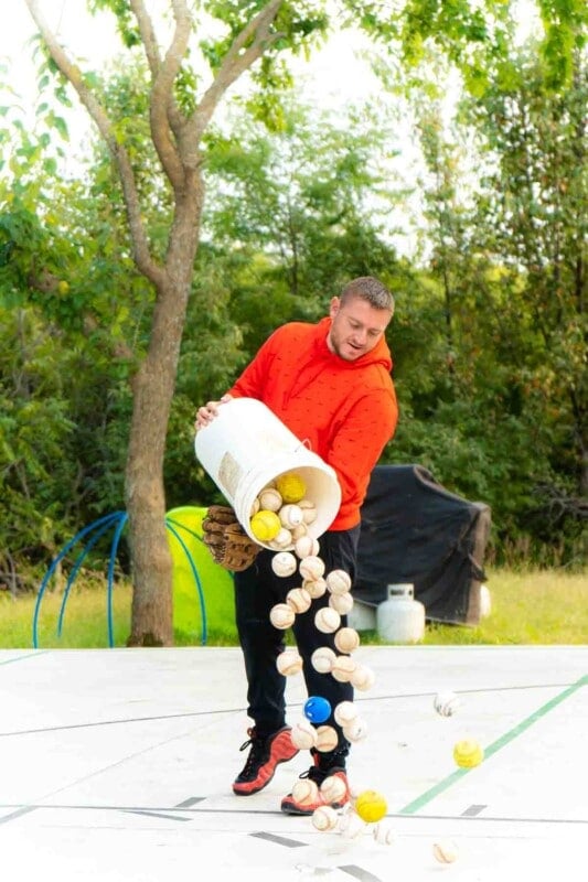Adult dumping a bucket of baseballs