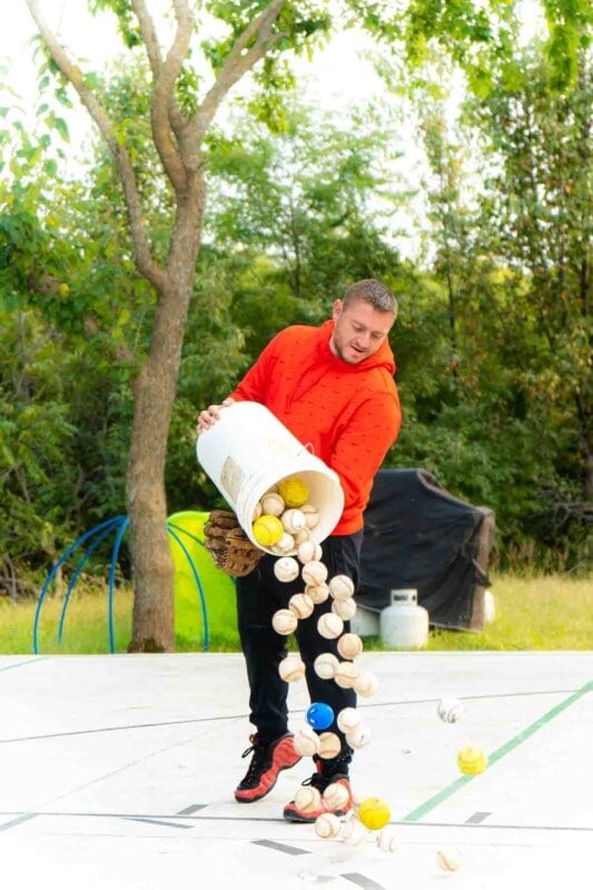 Adult dumping a bucket of baseballs 