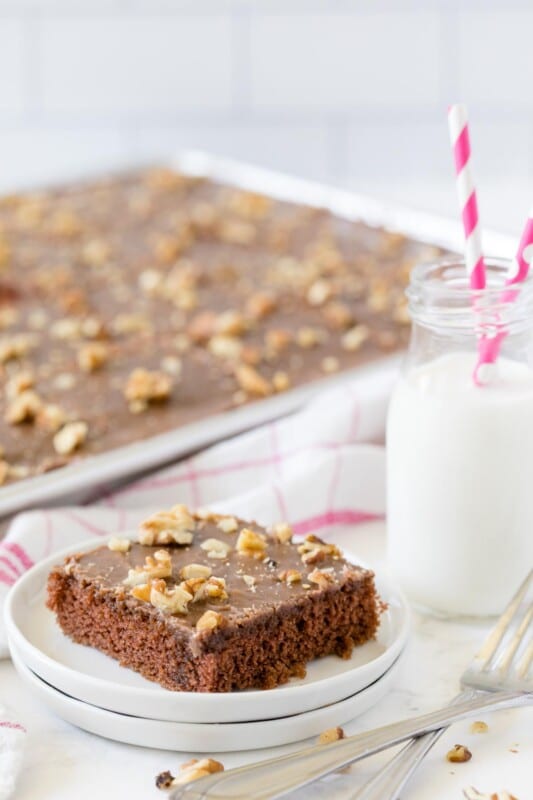 A piece of chocolate brownie on three stacked plates with a glass of milk with pink straws