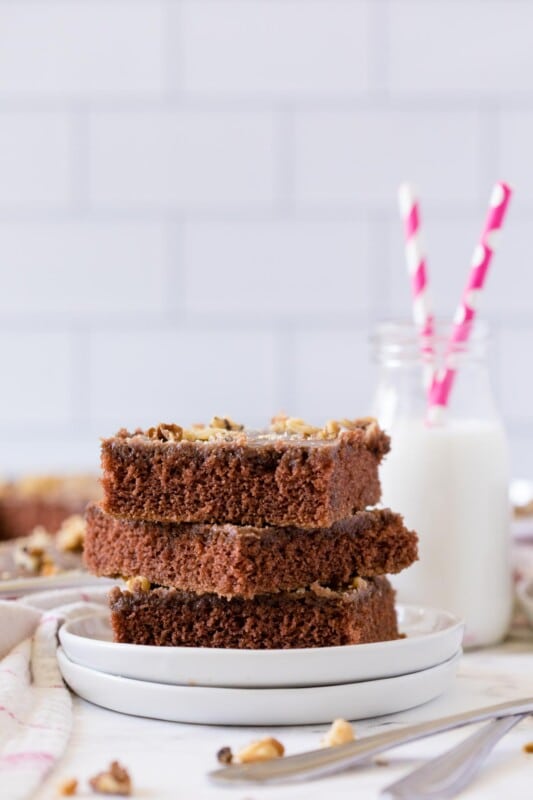 Three chocolate brownie cake slices stacked on top of each other with milk in the background