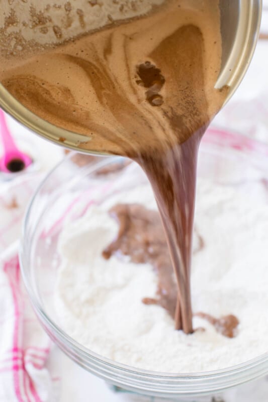 Metal pot pouring chocolate mixture to flour mixture in glass bowl