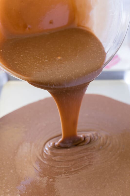 Glass bowl pouring chocolate brownie cake matter into sheet pan