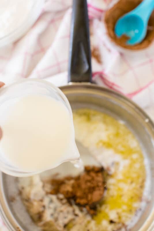 Glass measuring cup adding milk to melted butter in a pot