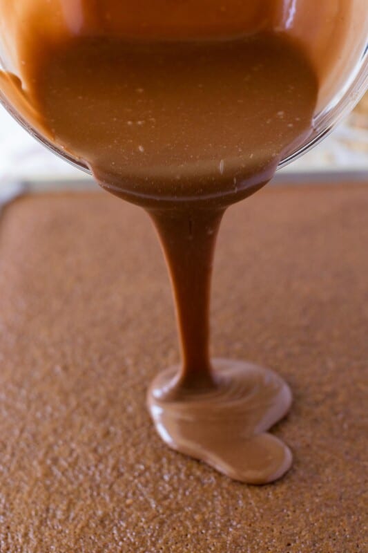 Glass bowl pouring icing onto chocolate brownie cake