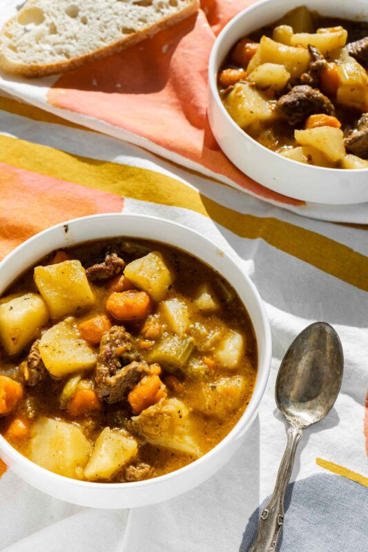 Top down photo of two white bowls with beef stew with potatoes inside
