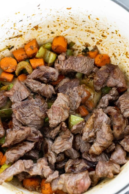 Browned beef on top of carrots and celery in a beef stew