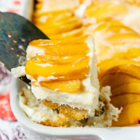 Spatula holding a piece of peach cake above a pan of peach cake