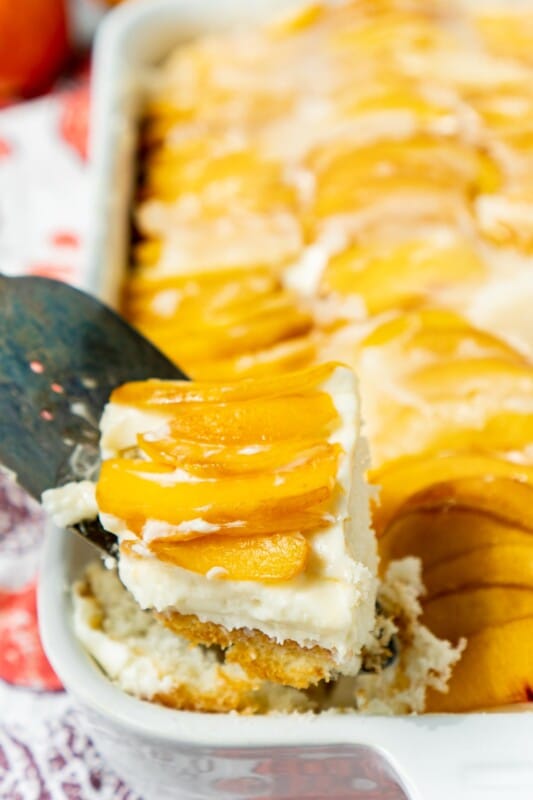 Spatula holding a piece of peach cake above a pan of peach cake