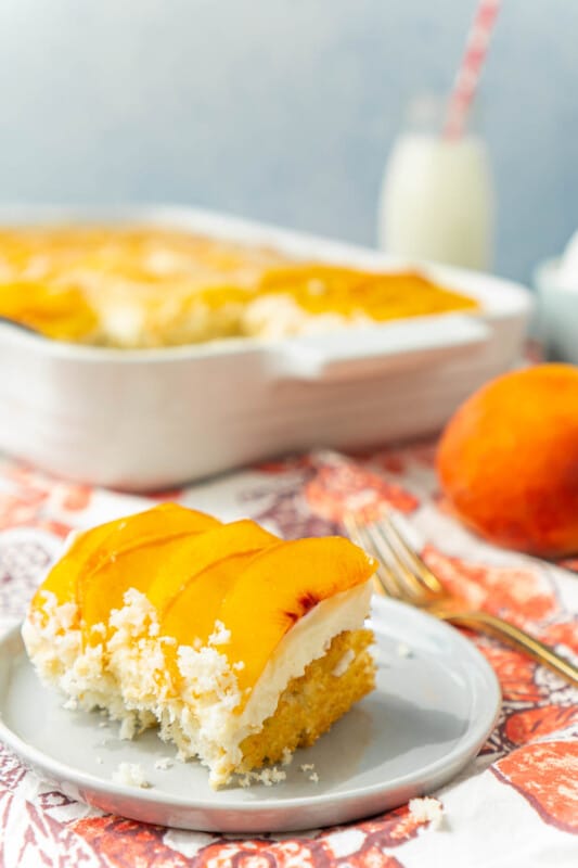 A slice of peach cake on a gray plate with a full peach cake in the background