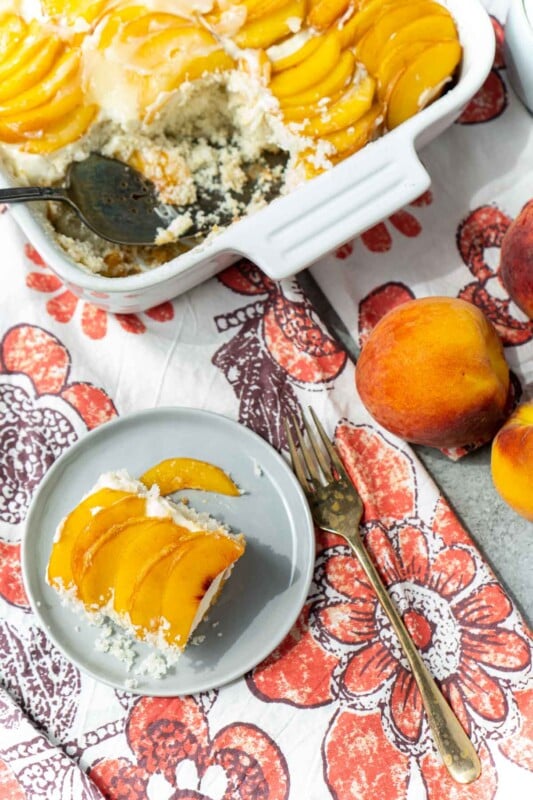 Top down shot of a piece of peach cake and an peach cake in a baking dish with a piece cut out