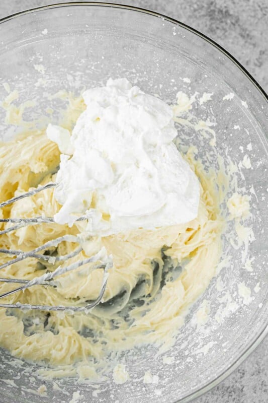 Glass bowl with metal beaters, a cream cheese frosting, and whipped cream