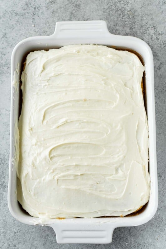 A cake with white creamy frosting in a white rectangle cake pan