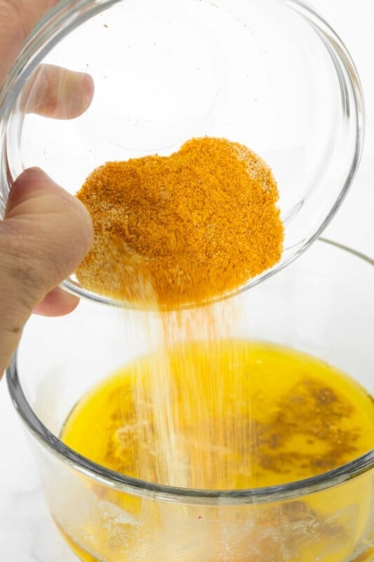 Woman's hand pouring seasonings into a bowl of melted butter