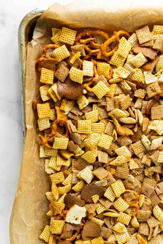 Homemade Chex Mix cooling on a parchment paper lined baking sheet