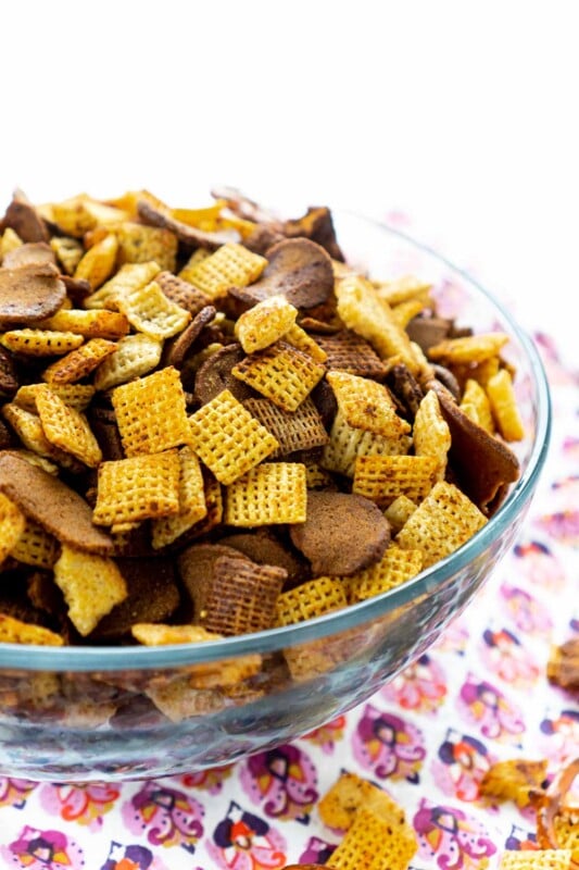 A glass bowl of homemade Chex Mix with a pink napkin underneath